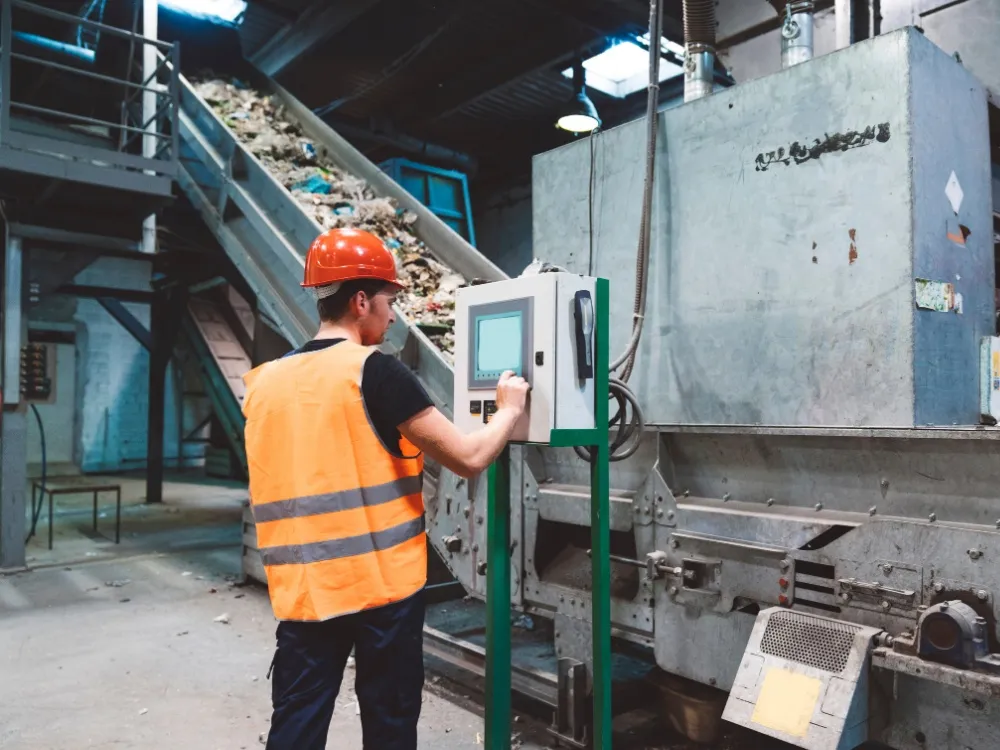 Worker in safety vest operating a control panel at a waste processing conveyor
