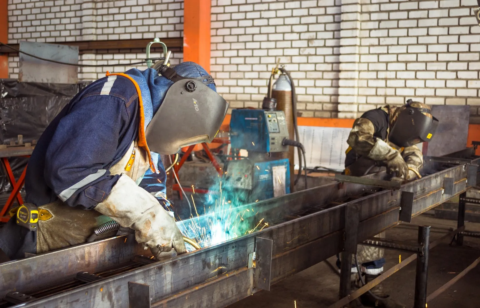 Two welders in protective gear welding a steel frame with bright arc and sparks