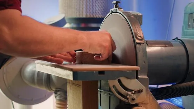 Worker sanding a metal part on a belt sanding machine